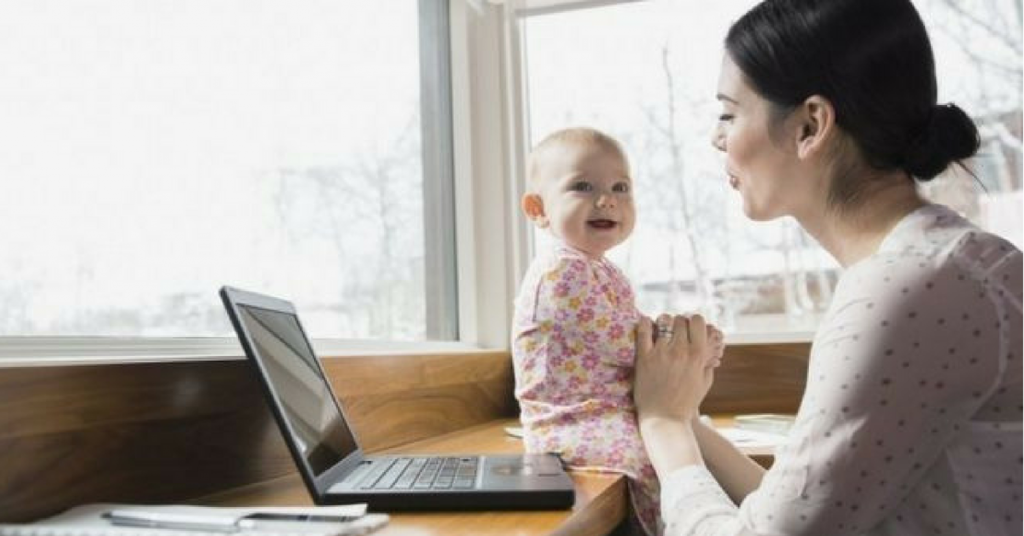 A mother working on her laptop while entertaining her young child.