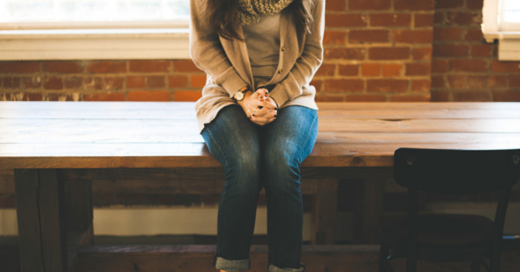 A young women sitting on a table with her hands folded.