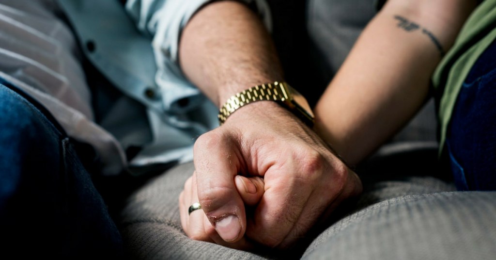 A couple holding hands while sitting on a couch.