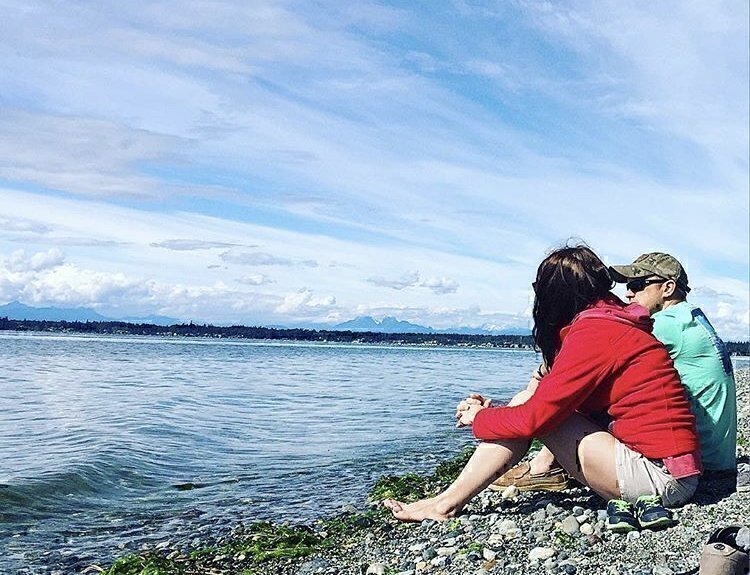 A couple seated on the edge of a lake talking to each other.