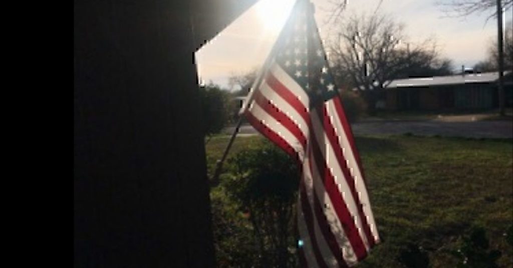 An American flag hanging in front of a small home.