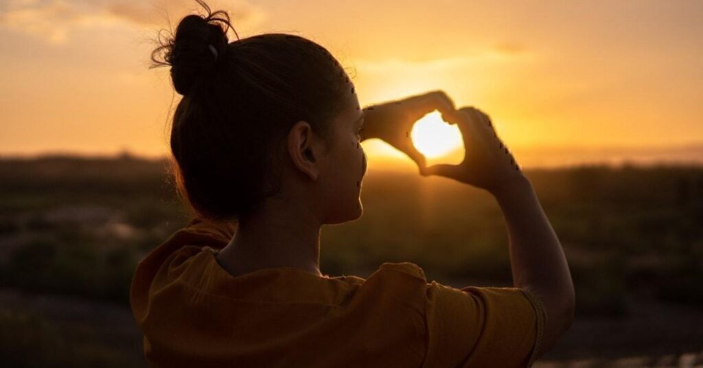 A women making a heart with her hands, and holding it up to the sun.