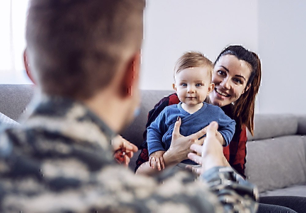 Military Spouse holds her child up to his dad for a hug