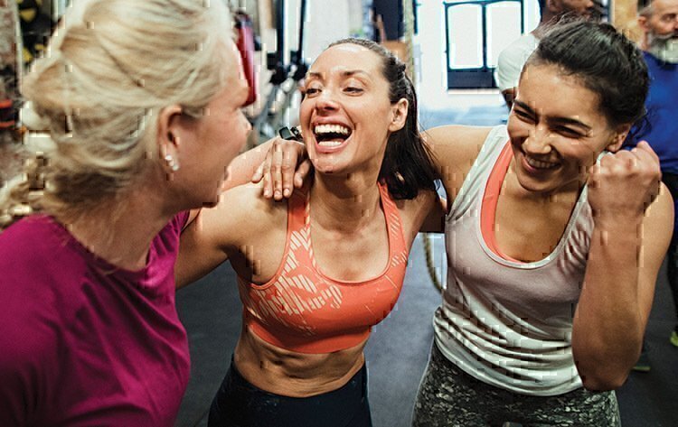 Three women smiling at each other and celebrating the completion of their workout. 