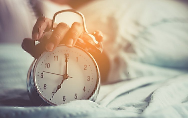 A women turning off of her alarm clock while rolling out of bed.