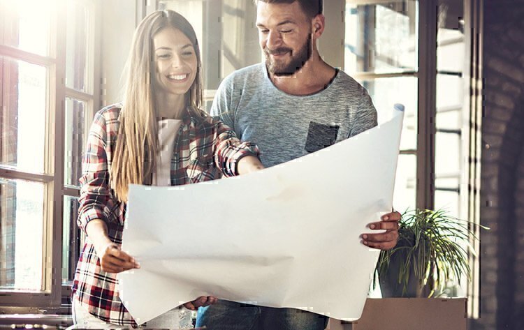 A man and a women smiling, while looking down at a large sheet of paper.