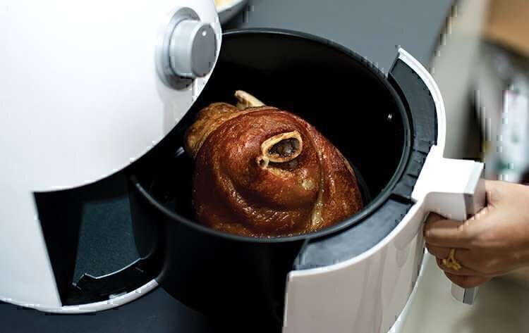 A women's hand pulling out meat from an air fryer.