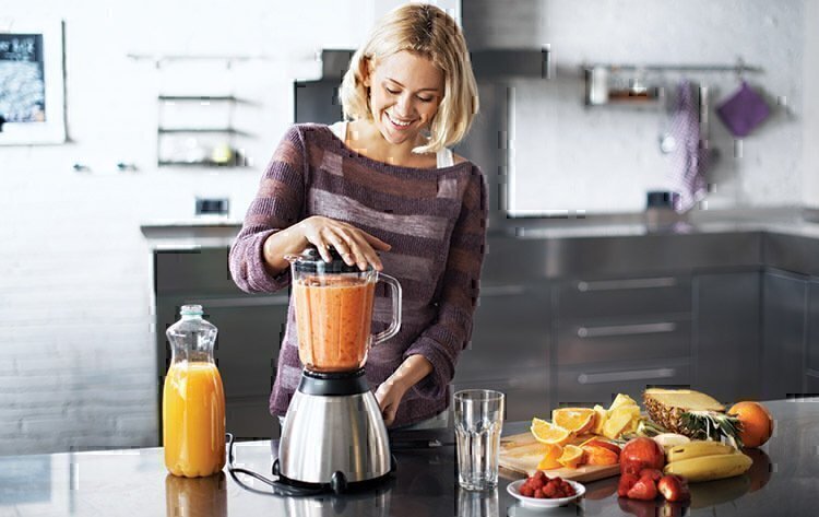 A women smiling while blending together her smoothie.