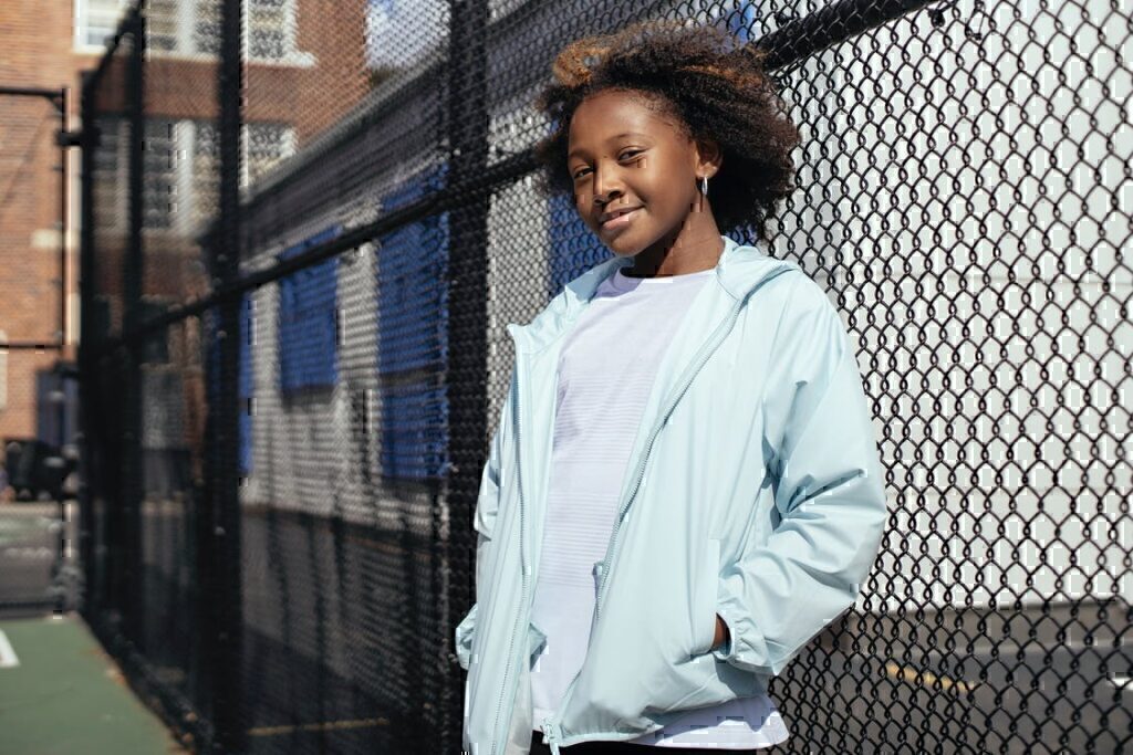 A young child sanding in front of a fence while smiling.