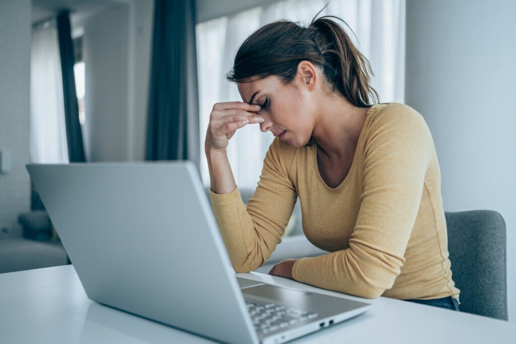 Stressed woman working from home. Frustrated businesswoman with head in hands sitting on the desk at home. Overworked young businesswoman sitting in front of laptop and holding head. Home office concept.